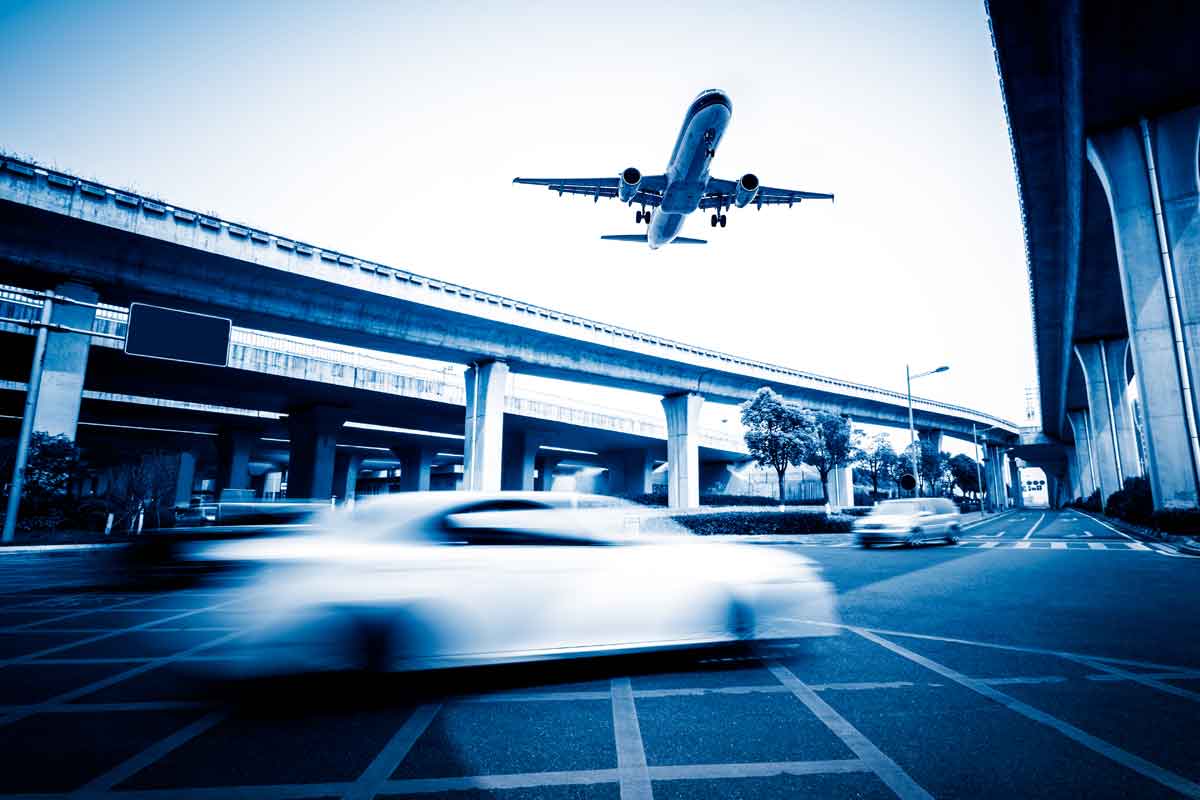 Un avion décolle au dessus d'un échangeur routier, une voiture passe au premier plan